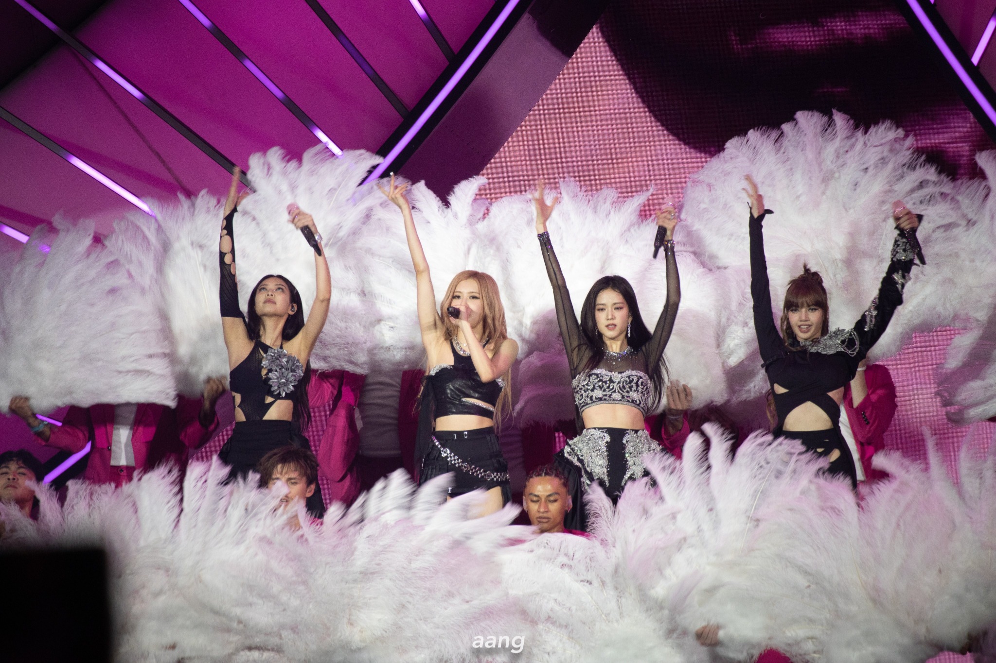 BLACKPINK sur scène en concert, entourées de plumes blanches et d’éclairages roses